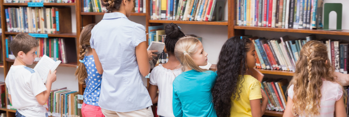 Students and Teacher selecting books from Library bookshelf