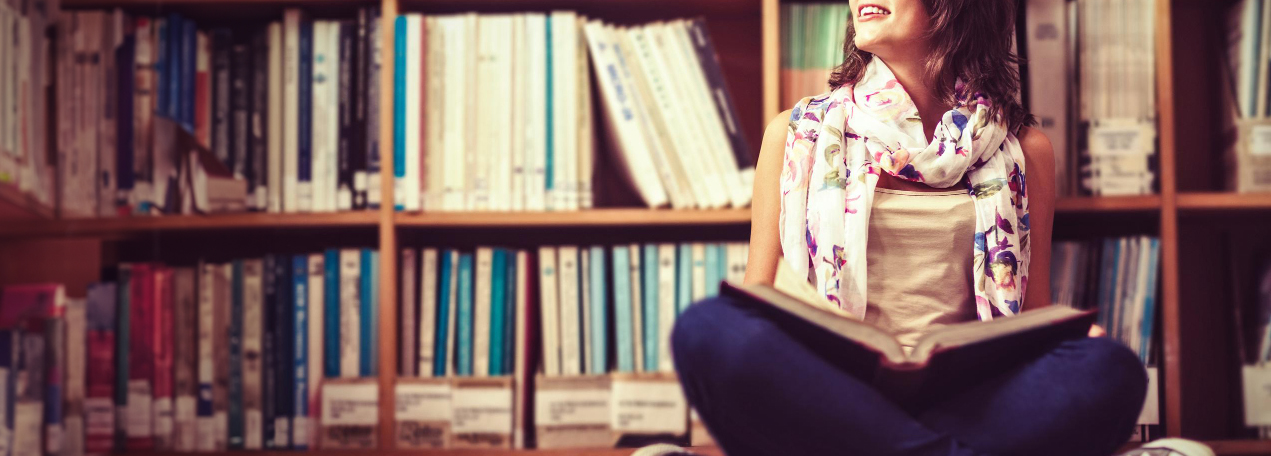 Woman reading a book in front of a book shelf